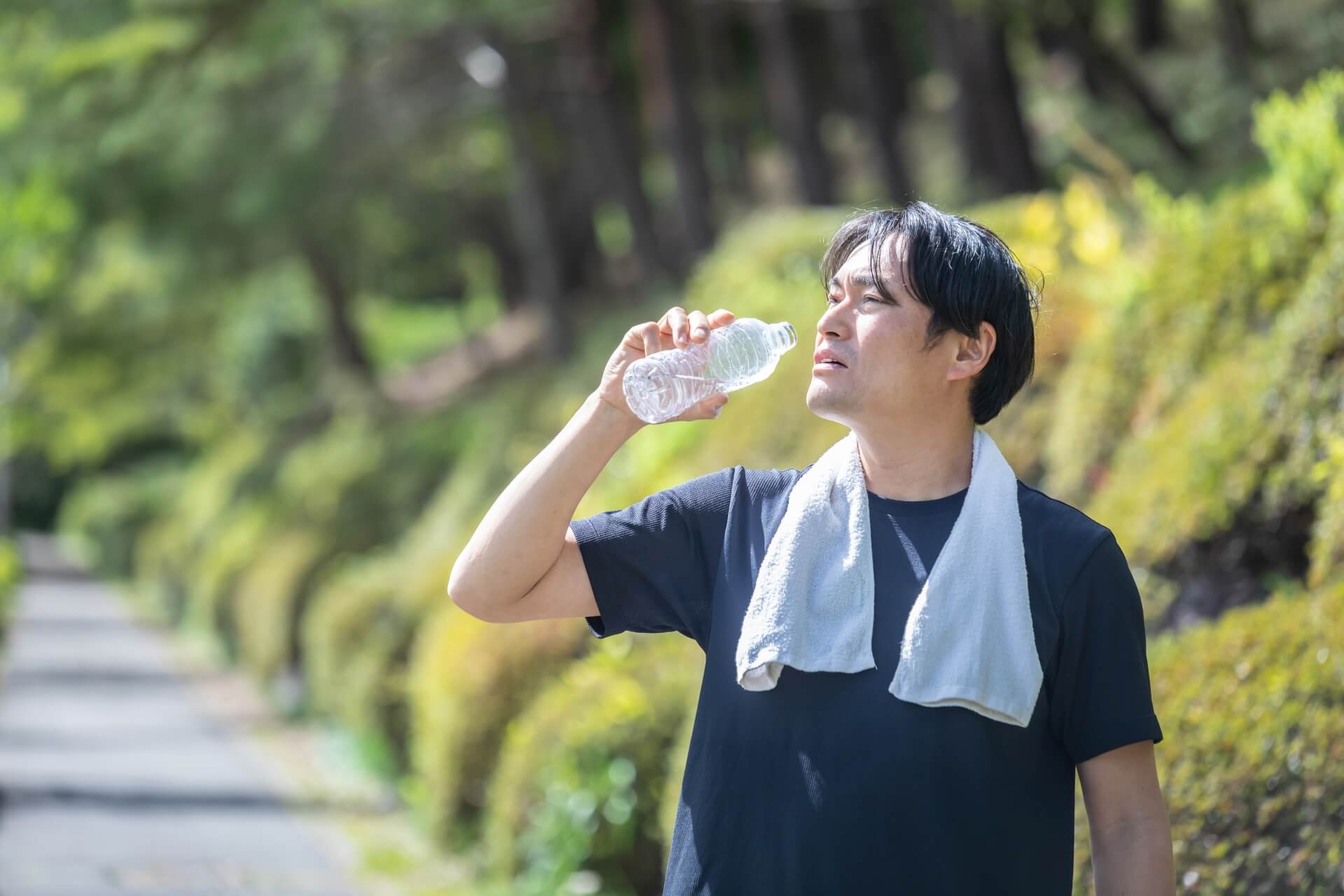 公園の小道で水を飲む黒い服の男性